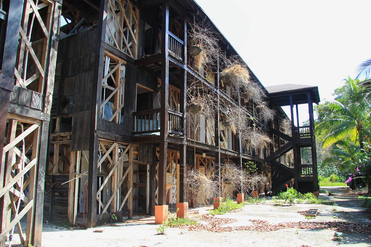 A guest room block with exterior siding and other components completely stripped. Hanging planters eerily hold unkempt vines.