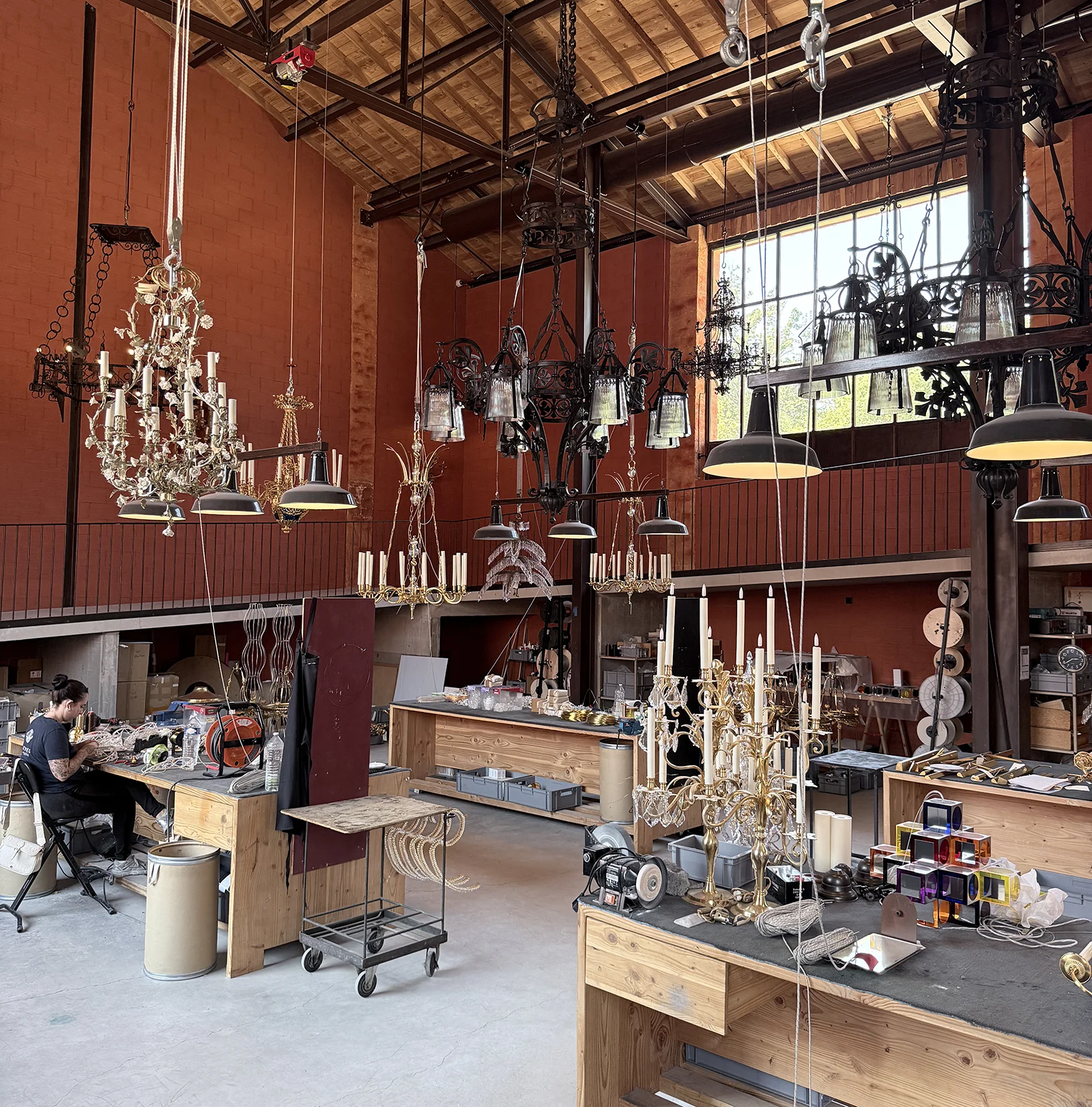 Interior of Mathieu Lustrerie chandelier workshop in Gargas, Provence, showing ornate chandeliers hanging from the ceiling and an artisan working at a wooden workbench