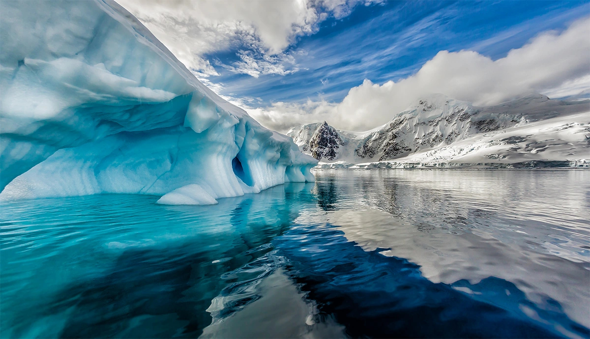 Massive blue iceberg floating in the still waters of Andord Bay, Antarctic Peninsula, with snow-covered mountains reflected in the foreground
