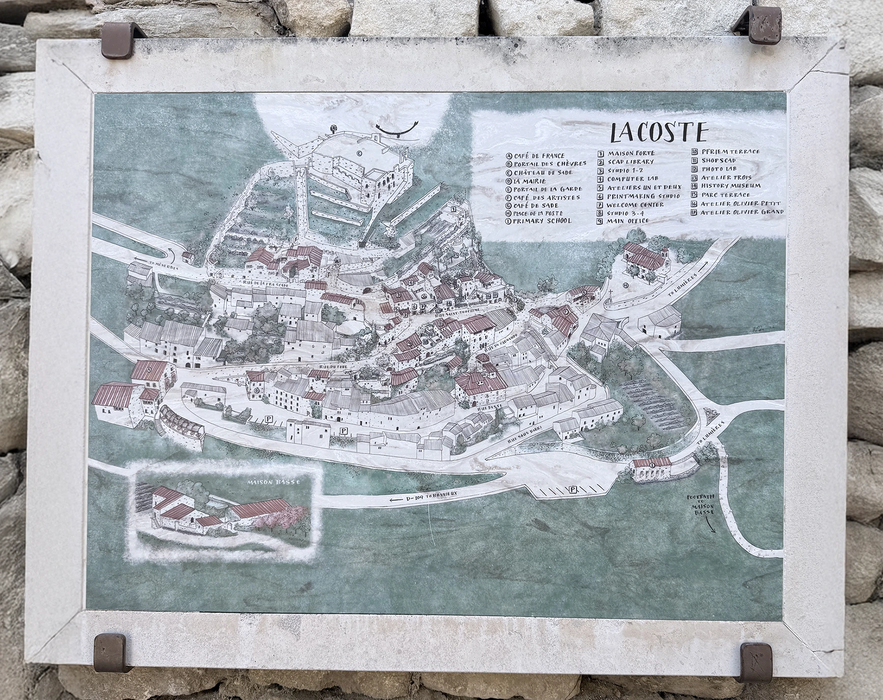 Illustrated map of Lacoste village in Provence showing Château de Sade, SCAD campus buildings, and village streets, mounted on a stone wall