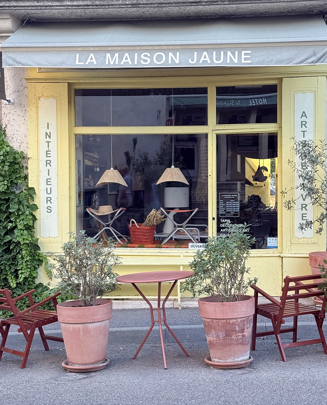 La Maison Jaune shop front in Sault, Provence, with yellow painted windows, terracotta pots, and red bistro chairs on an empty street