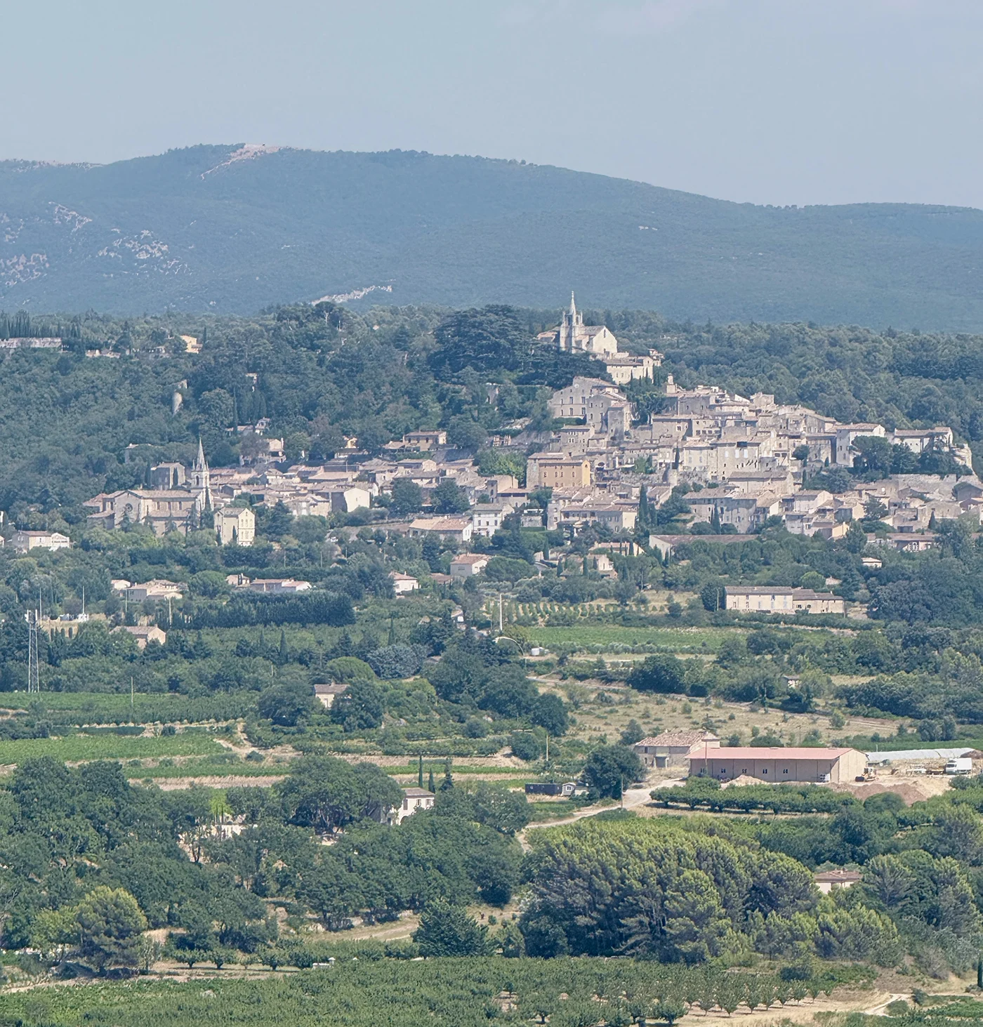 View of Bonnieux hilltop village in Provence as seen from Lacoste, with vineyards and farmland in the valley below and the Luberon mountains behind